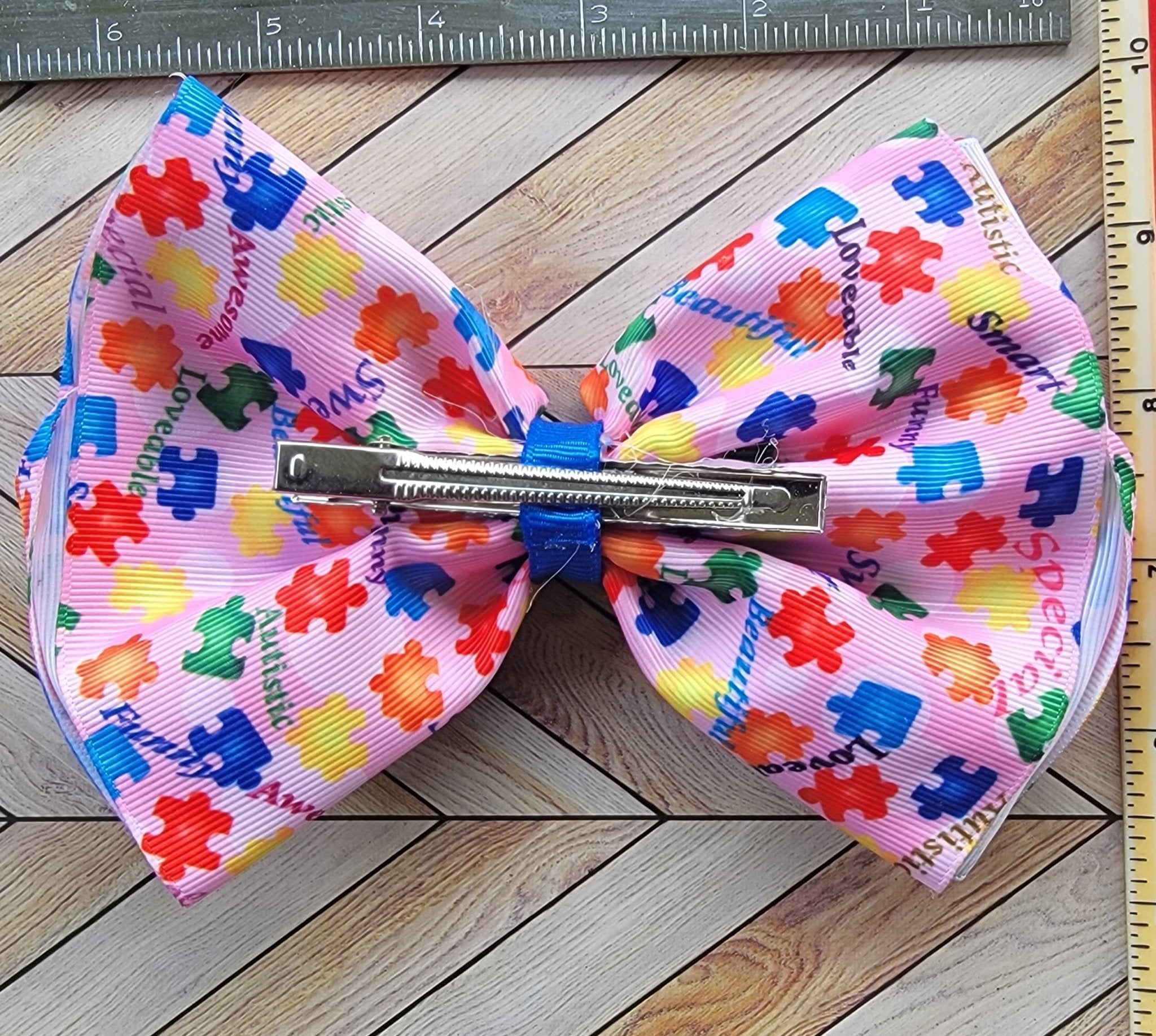 Colorful bow with puzzle piece pattern on a wooden surface with a ruler for scale.