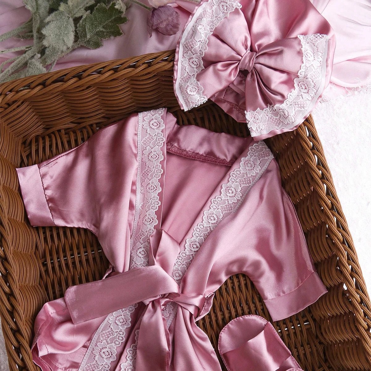 Pink satin robe with lace trim and matching headband on a woven basket