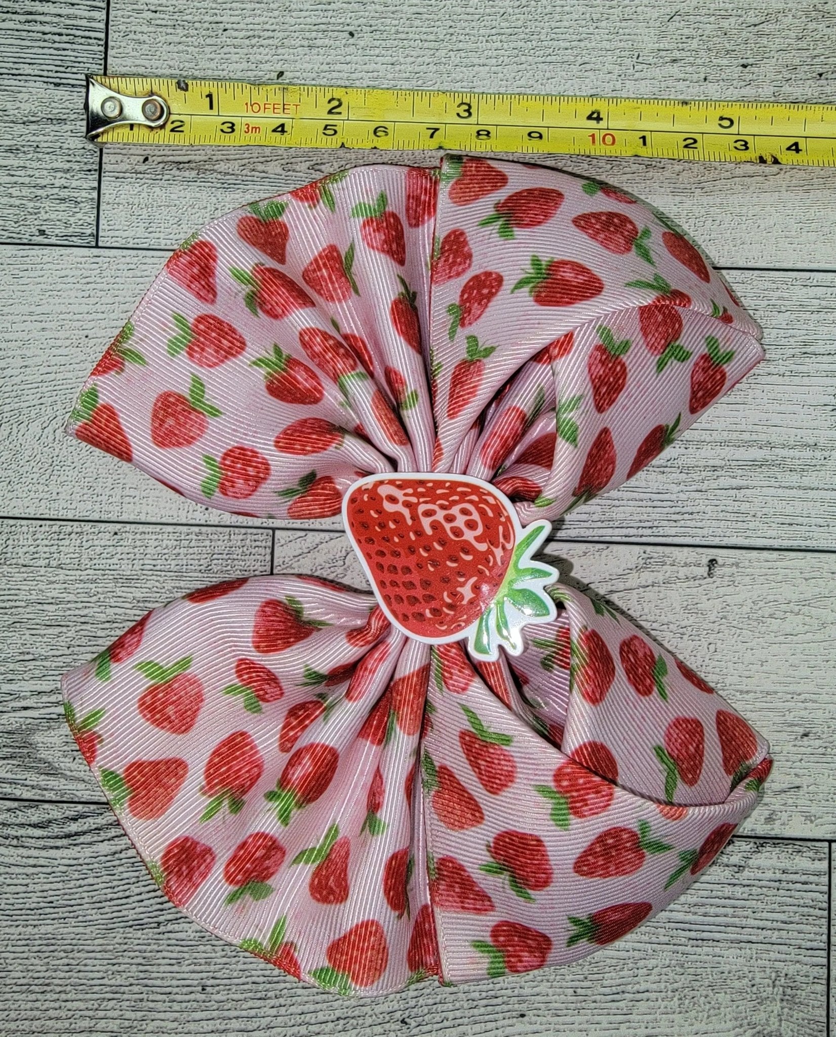 Large fabric bow with strawberry pattern next to a measuring tape on a wooden surface