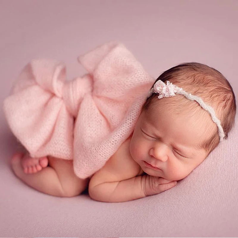 Newborn baby wrapped in a pink blanket with a matching headband on a pink background