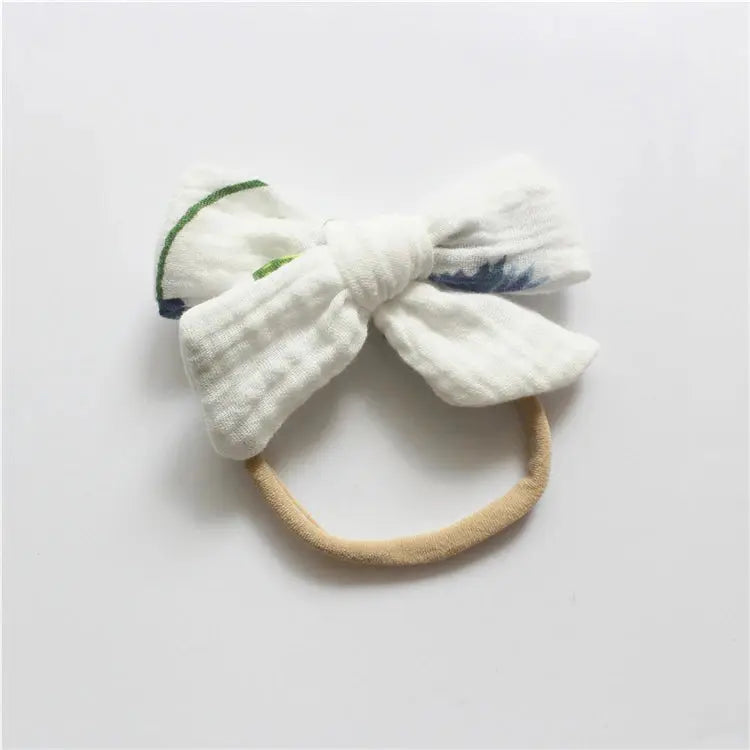 White bow-shaped headband with a beige band on a light gray background