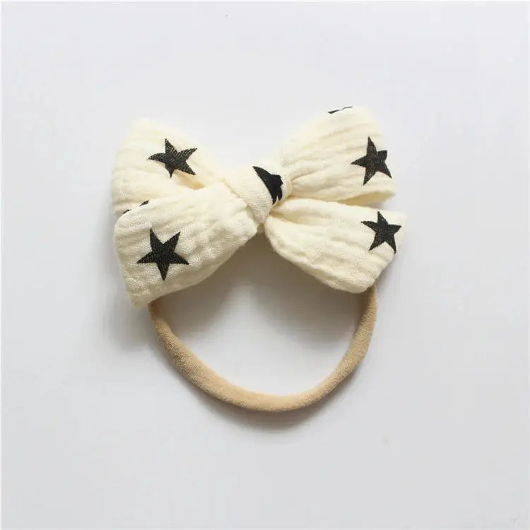Cream-colored headband with large bow and black star details on a light gray background
