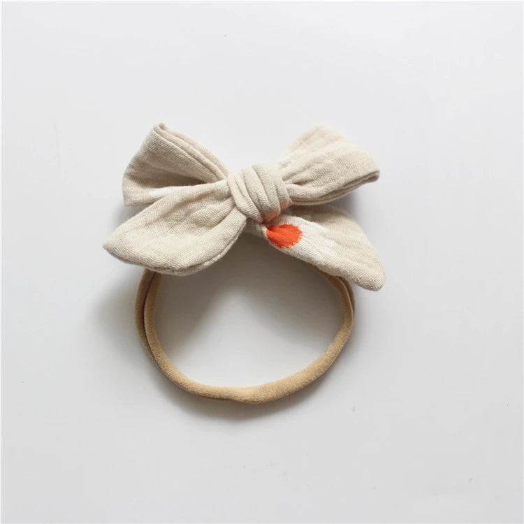 Beige headband with a large bow and orange center on a light gray background