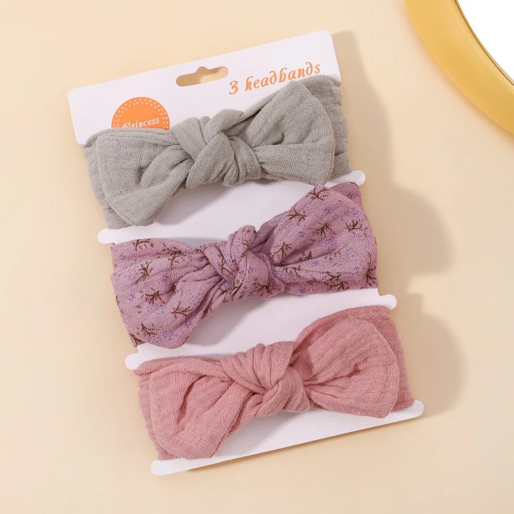 Three knotted headbands in gray, pink, and red on a beige background