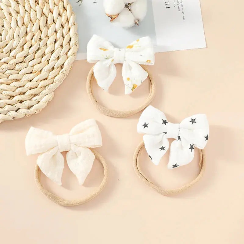 Three headbands with white bows on a beige surface with a woven basket and cotton flowers in the background.