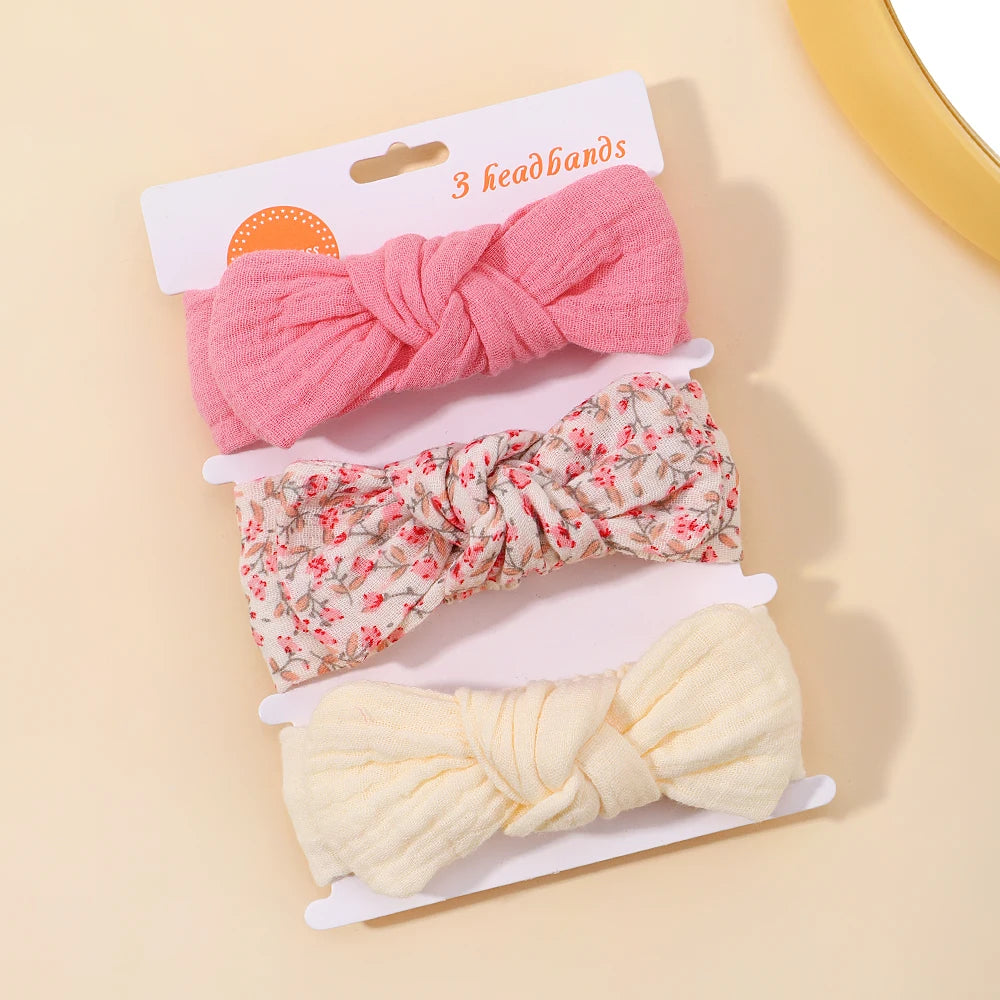 Set of three knotted headbands in pink, floral, and white on a beige background