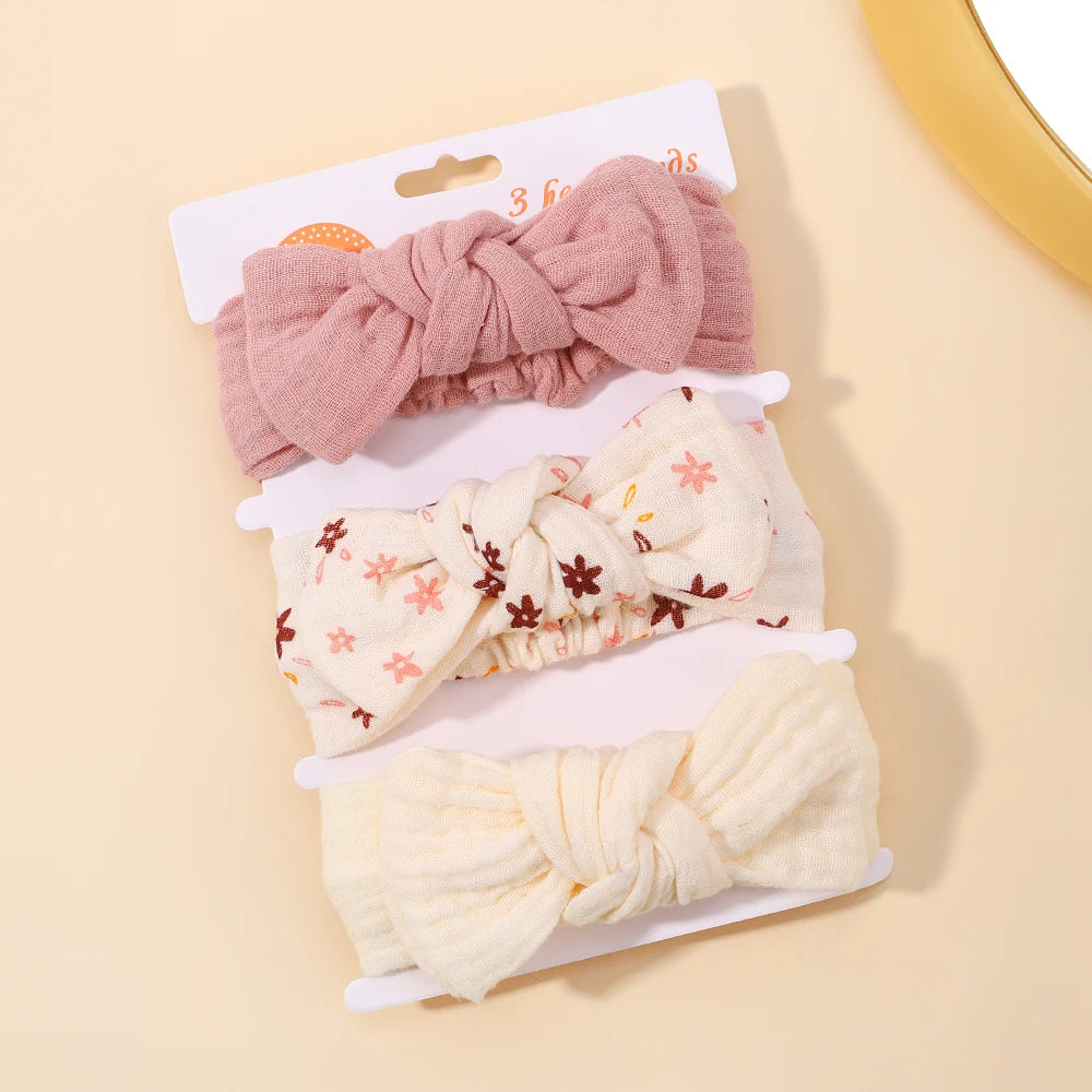 Set of three knotted hair bows in pink, cream with floral pattern, and white on a beige background.