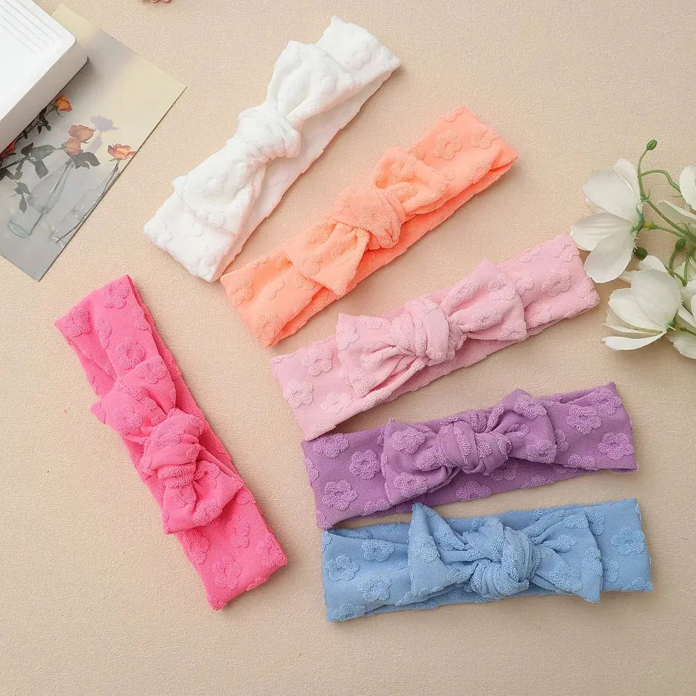 Set of colorful lace headbands on a beige surface with flowers and a book in the background.