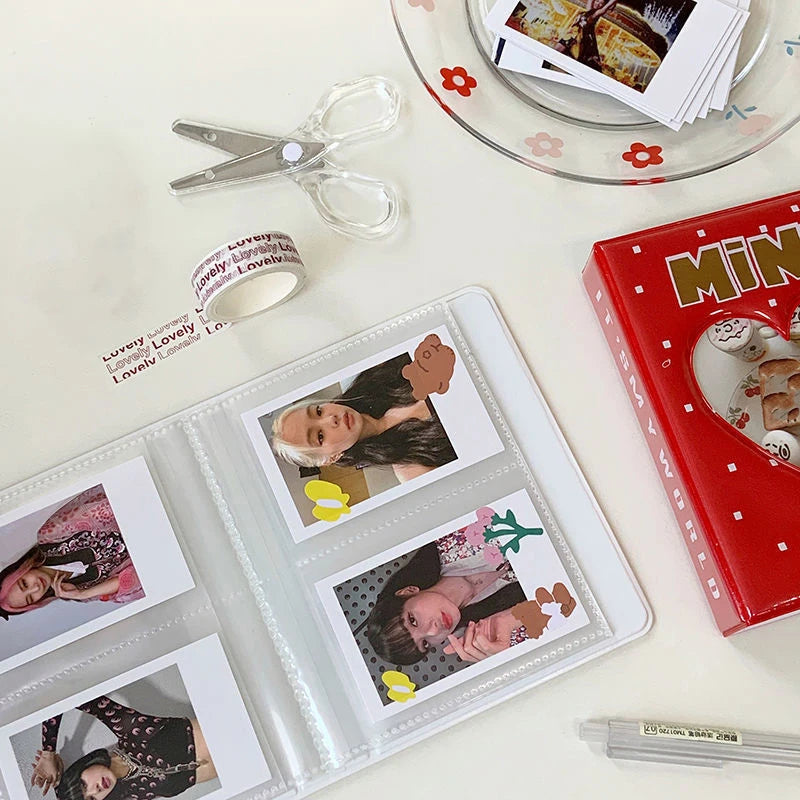 Photo album with printed photos, scissors, tape, and a book on a light surface.