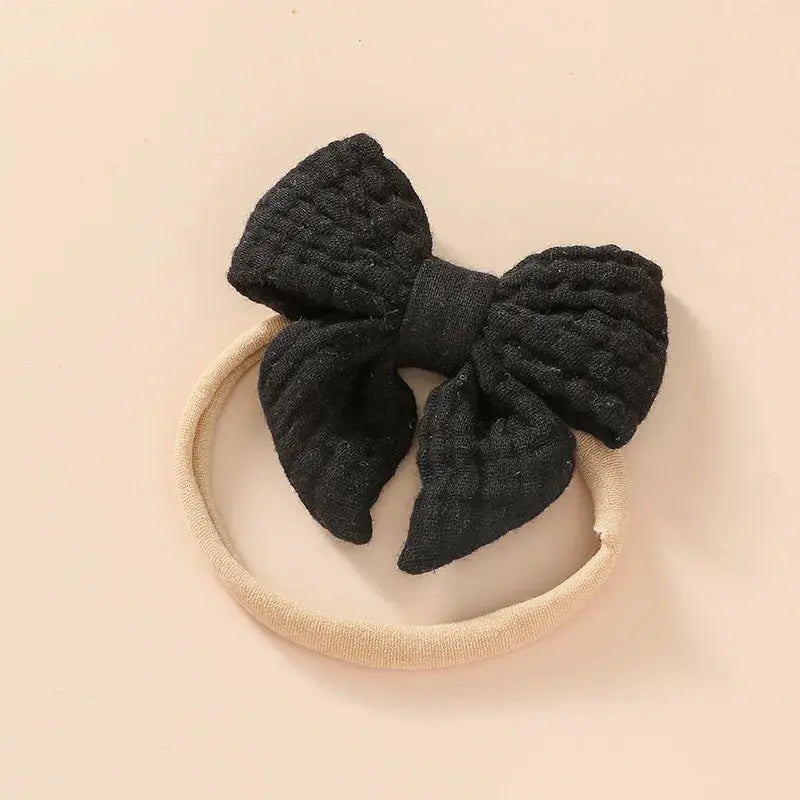 Black textured bow on a beige headband against a beige background