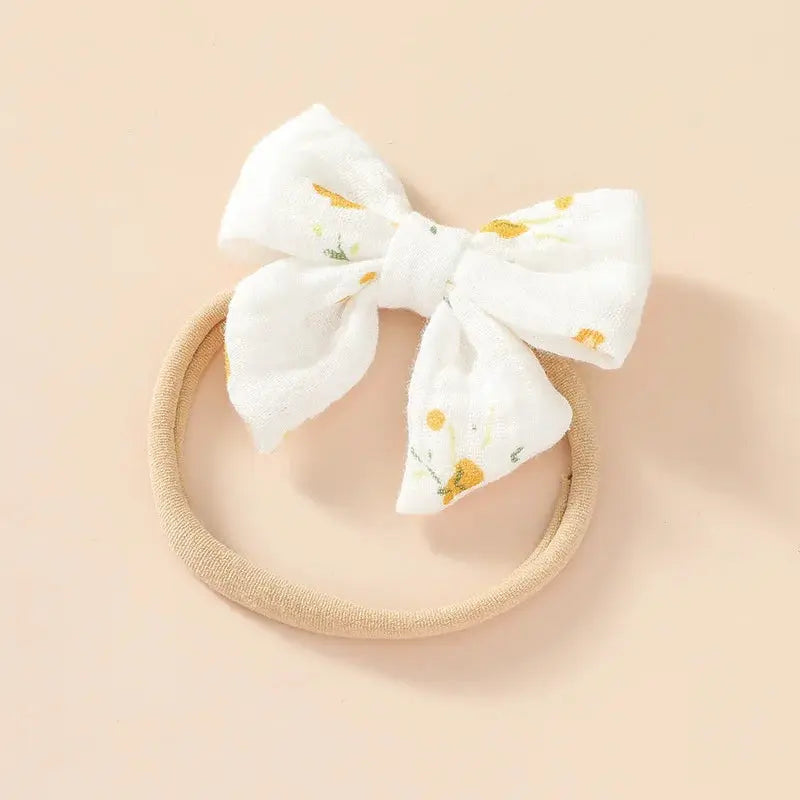 White floral bow on a beige headband against a beige background
