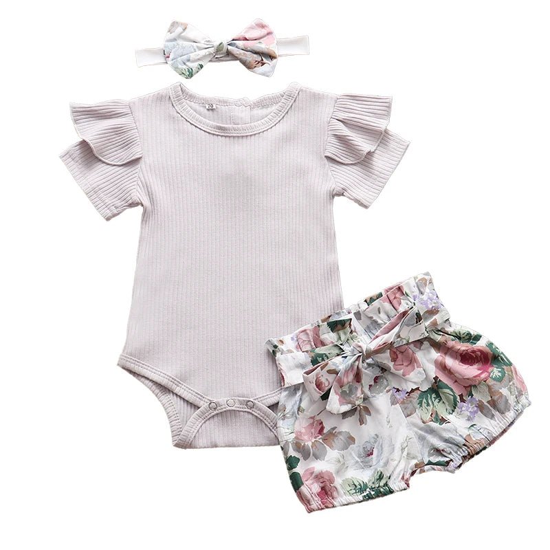 Baby outfit set with ruffled onesie, floral shorts, and headband on a white background