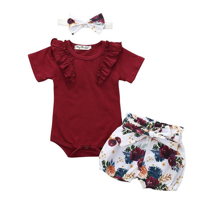 Baby outfit set with red romper, floral bloomers, and headband on a white background