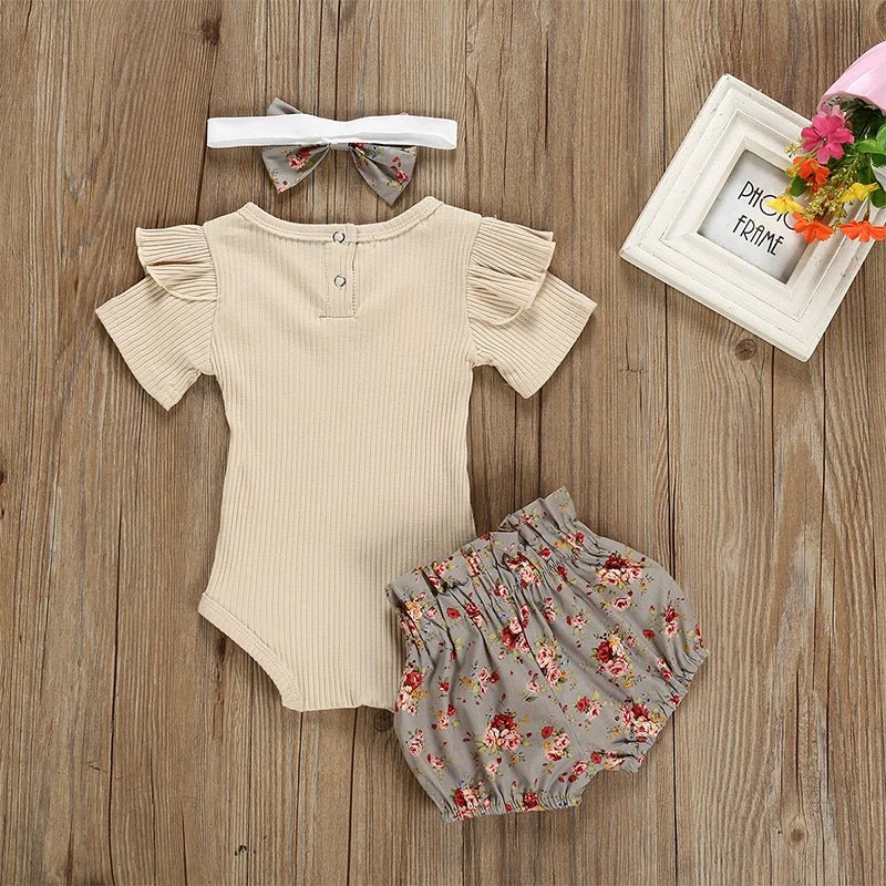 Baby outfit with beige romper, floral bloomers, and headband on a wooden surface.