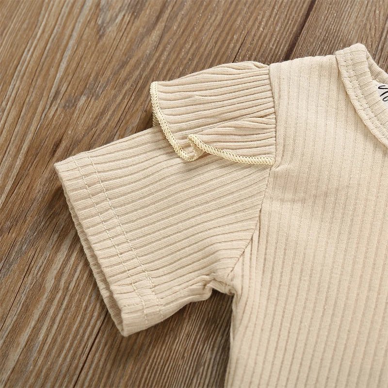 Beige ribbed baby romper on a wooden surface