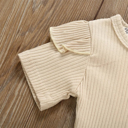 Beige ribbed baby romper on a wooden surface