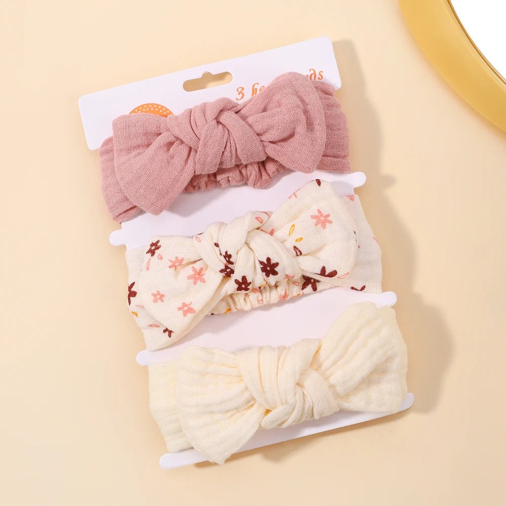 Set of three knotted hair bows in pink, cream with floral pattern, and white on a beige background.