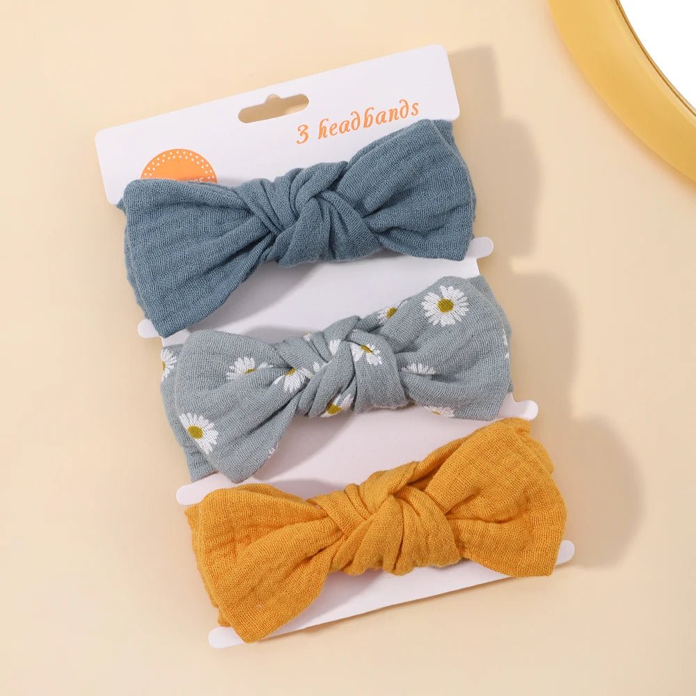 Three knotted hair bows in blue, gray with floral pattern, and yellow on a beige background.