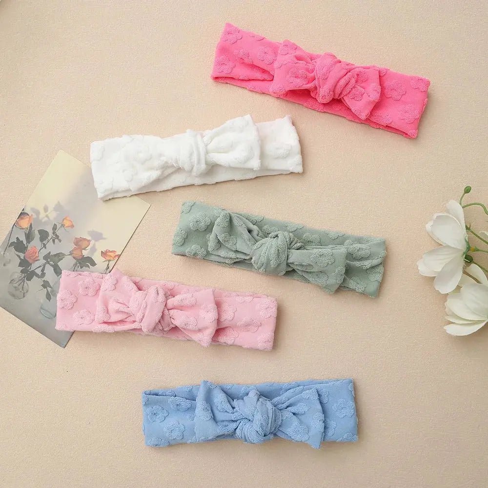 Set of five colorful knotted headbands on a beige surface with floral decorations.