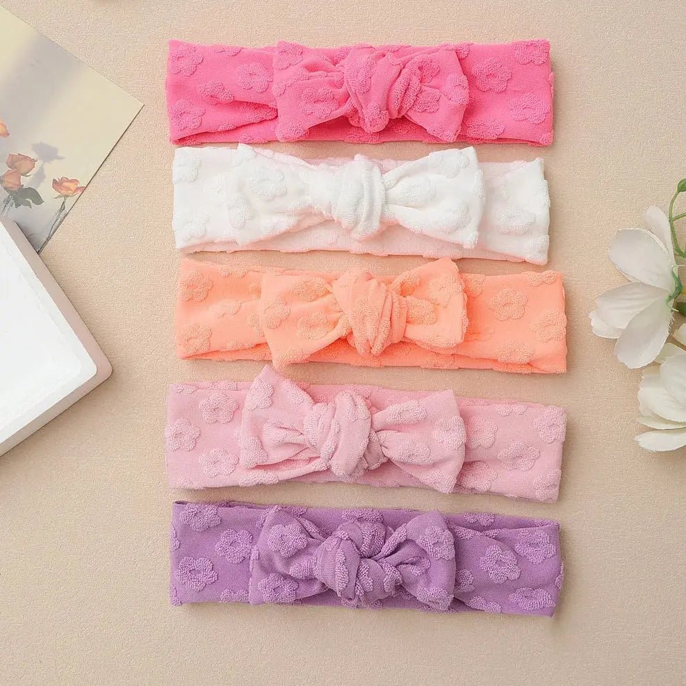Set of five colorful lace headbands on a beige surface with flowers.