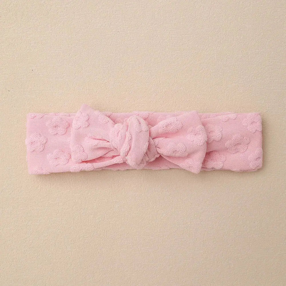 Pink textured headband with a bow on a beige background
