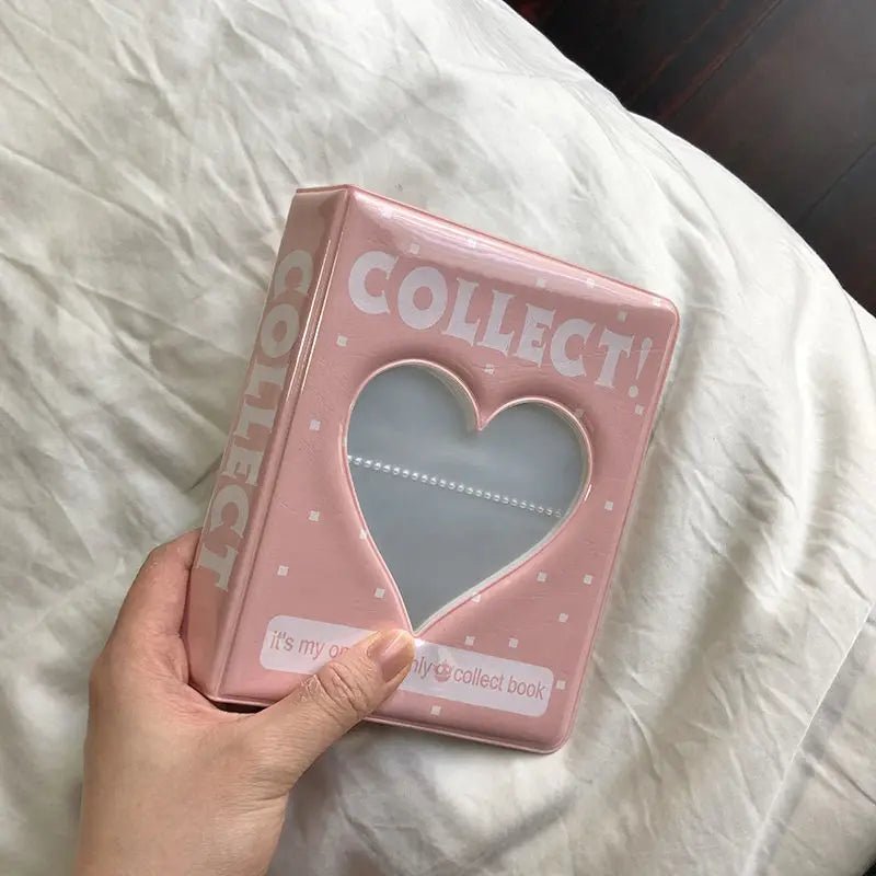 Pink heart-shaped photo album with 'COLLECT' text held by a hand on a white surface