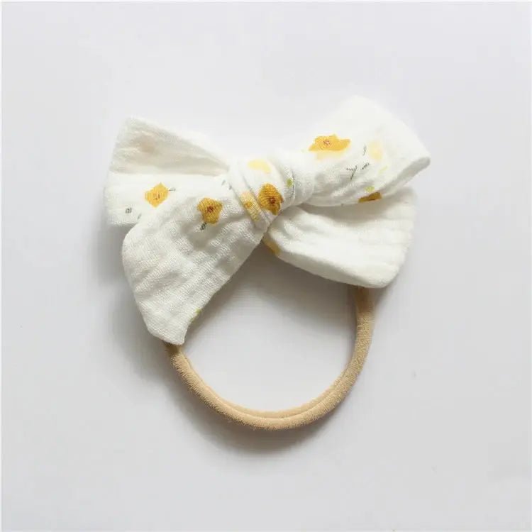 White bow-shaped headband with yellow floral patterns on a light gray background