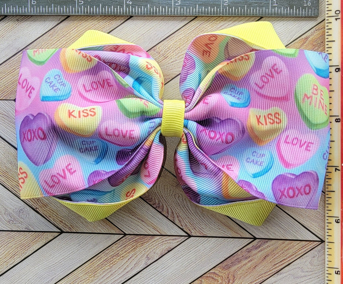 Colorful bow with candy heart pattern on a wooden surface with a ruler for scale.