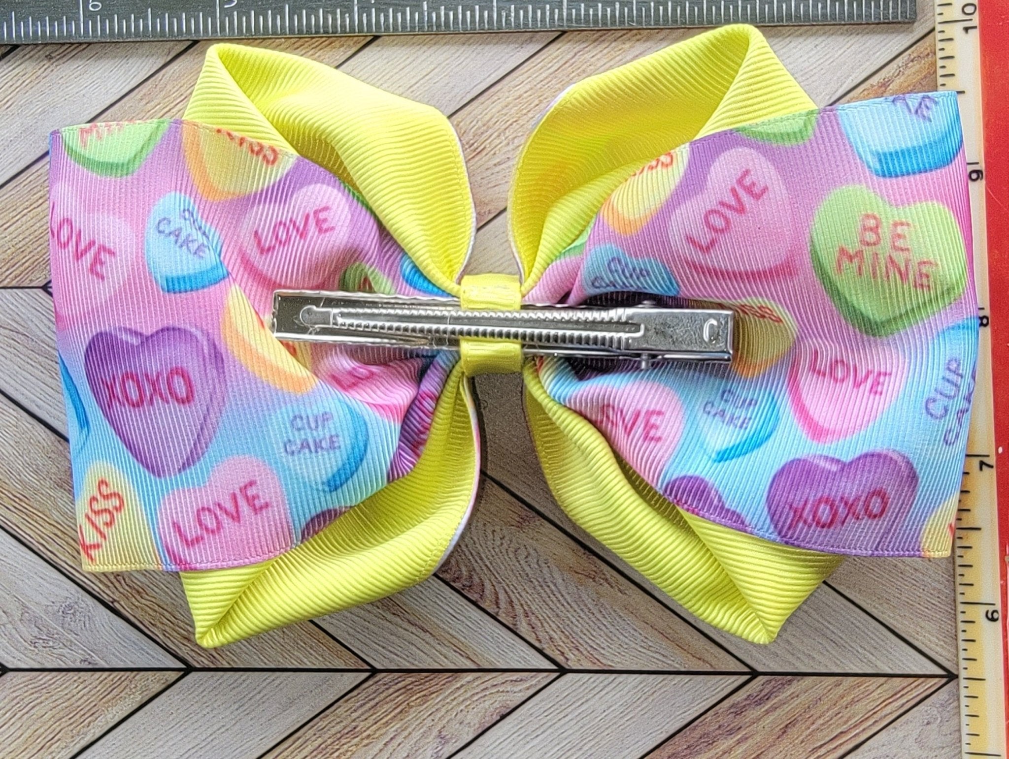 Colorful hair bow with heart patterns on a wooden surface next to a ruler.