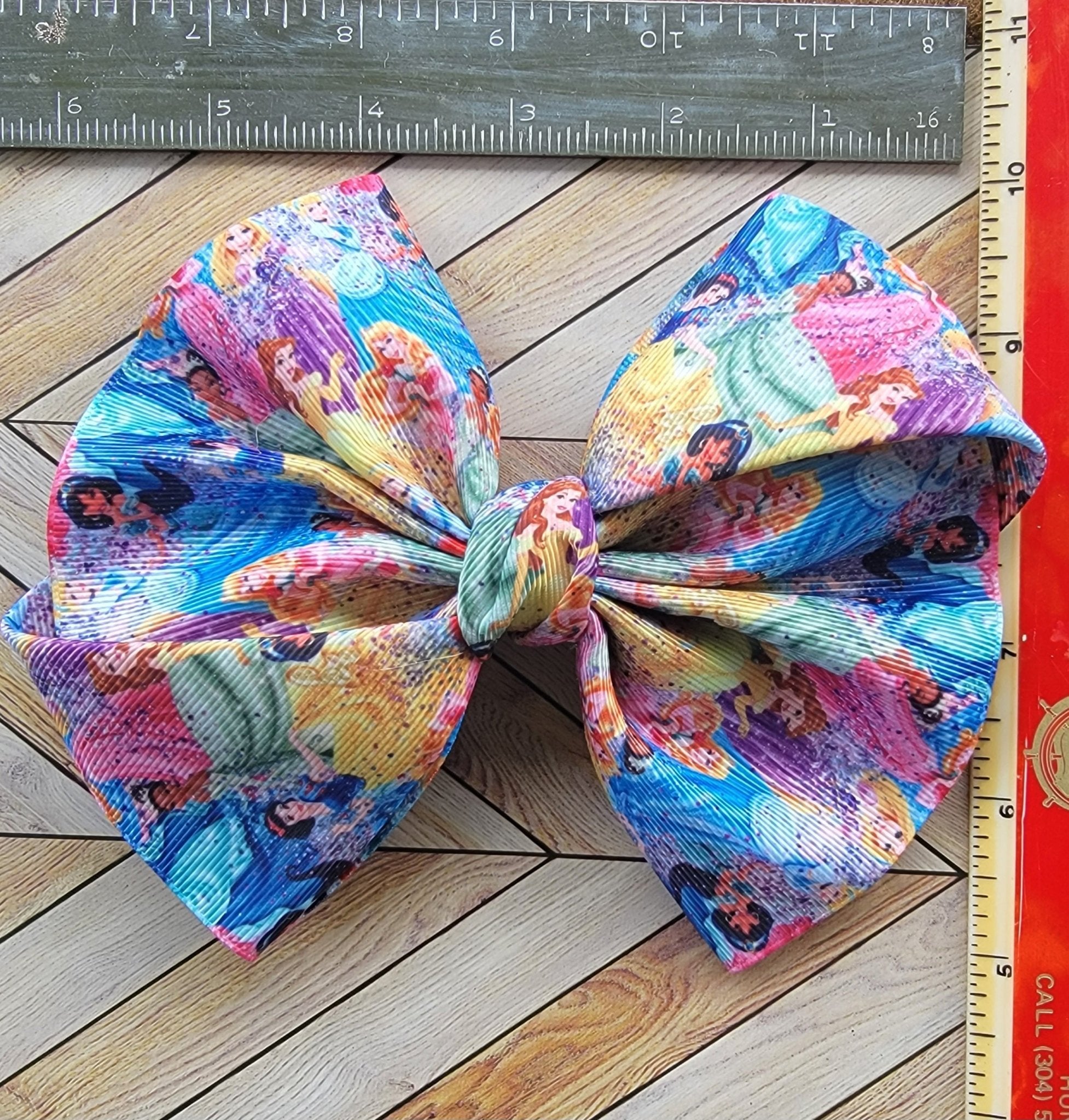 Colorful fabric bow with cartoon characters on a wooden surface next to a ruler.