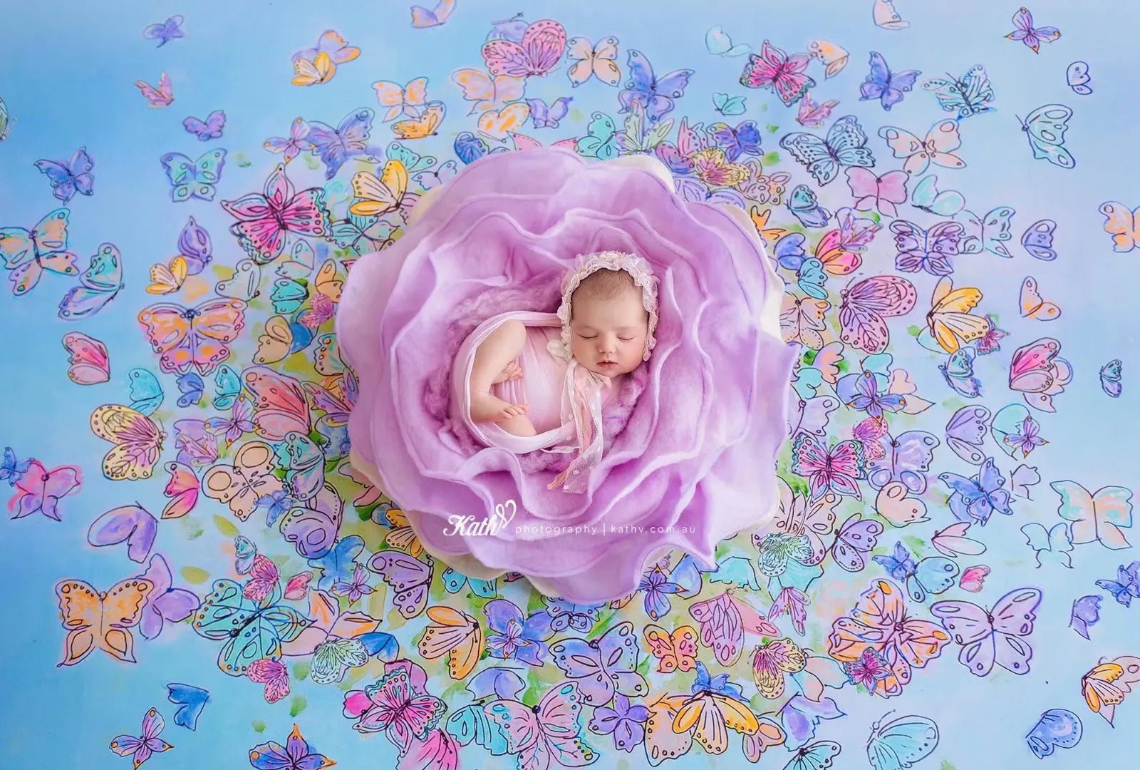 Newborn baby in a purple floral arrangement with colorful butterflies on a blue background
