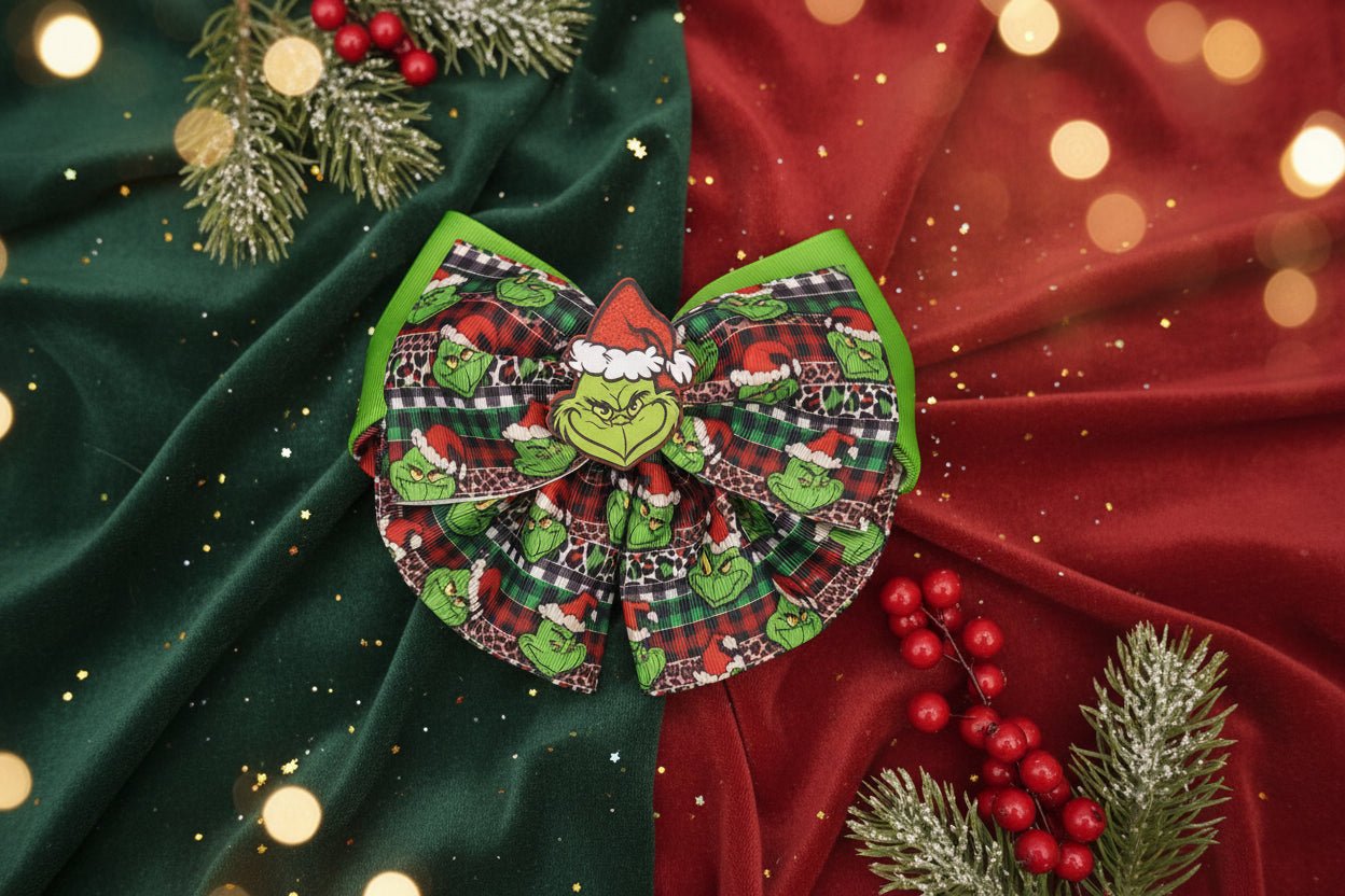 A Christmas-themed hair bow featuring a Grinch face, green Grinch characters, red and black plaid patterns, and green trim, displayed on a light gray textured surface.