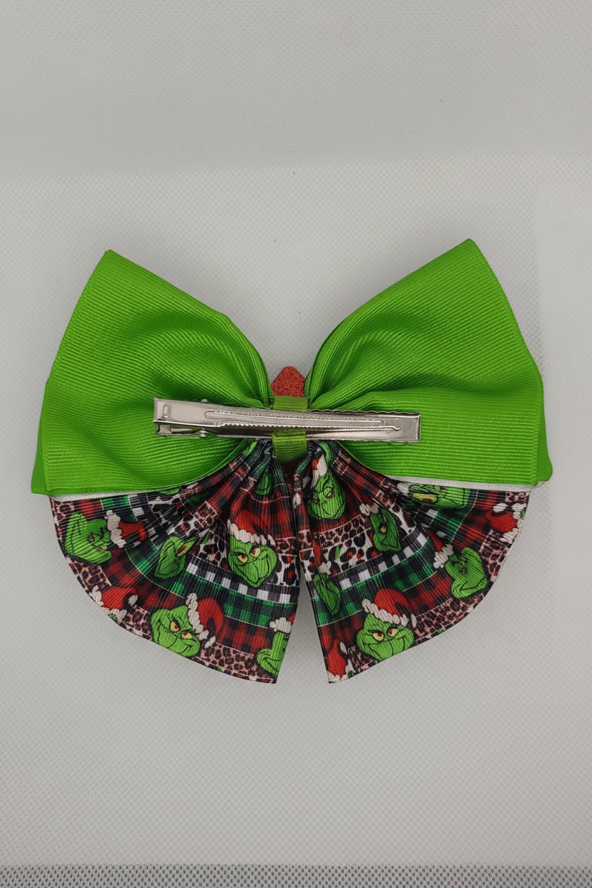 A Christmas-themed hair bow accessory featuring a bright green grosgrain ribbon half and a patterned fabric half with the Grinch, plaid, and Santa hats, secured with a silver metal claw clip.