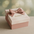 A square gift box with a dusty pink base and lid, decorated with a matching pink satin bow and embossed floral patterns. The lid features the brand name 'BowBabys' in gold lettering.