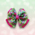 A colorful hair bow with a cartoon avocado pattern, pink trim, and a pink center