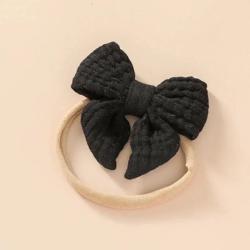 Black textured bow on a beige headband against a beige background