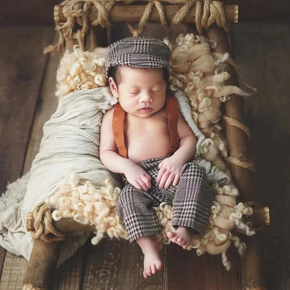 Newborn baby in plaid outfit sleeping in a wooden crib with soft bedding.