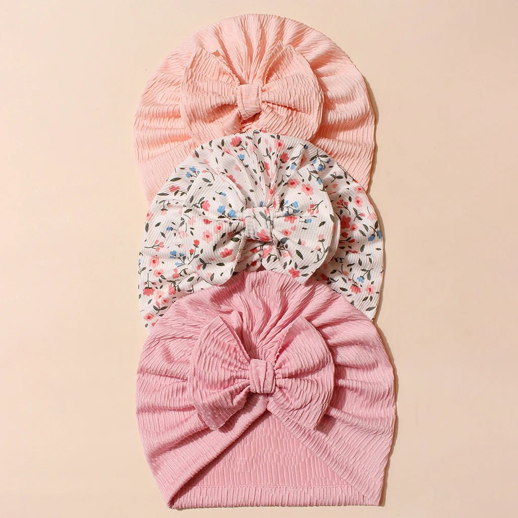 Three pink baby turbans with floral patterns on a beige background