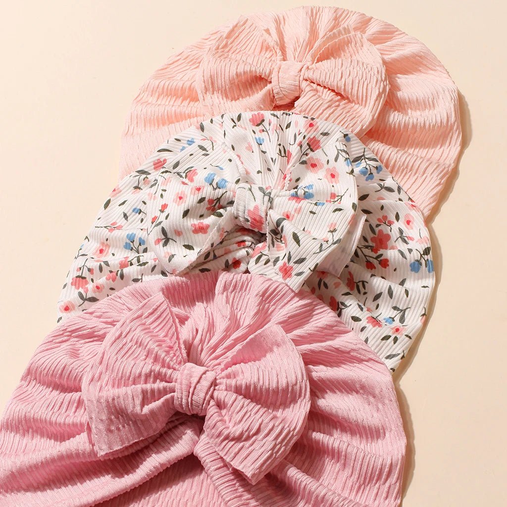 Two pink baby turbans with floral patterns on a beige background