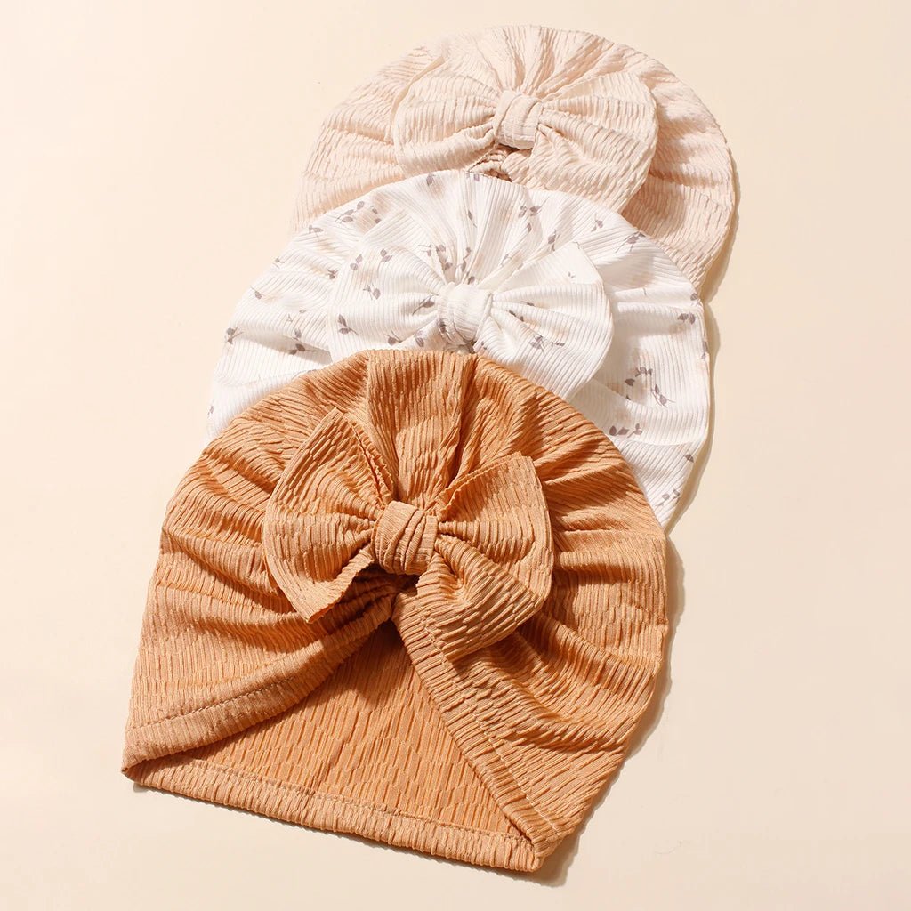 Three baby turbans in beige, white, and brown on a beige background