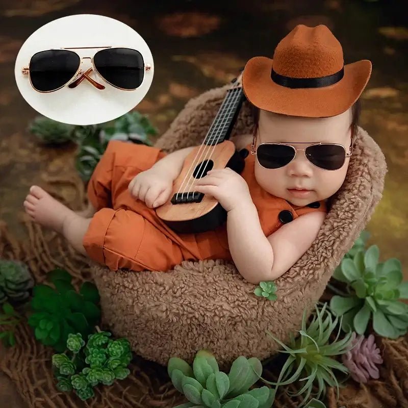 Baby in cowboy outfit with guitar and sunglasses, surrounded by plants