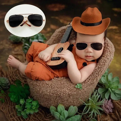 Baby in cowboy outfit with guitar and sunglasses, surrounded by plants