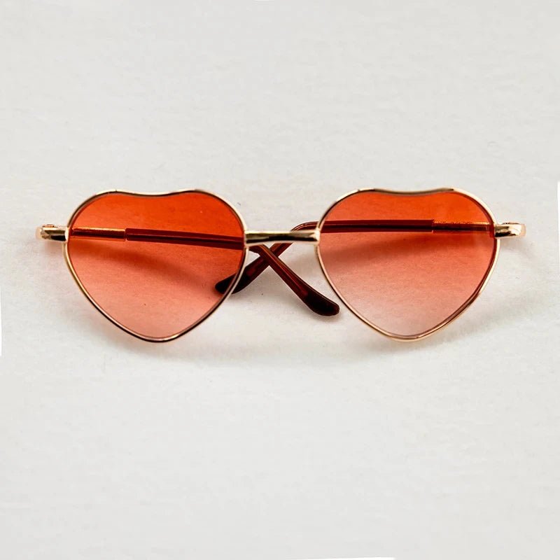Heart-shaped sunglasses with orange lenses on a light gray background