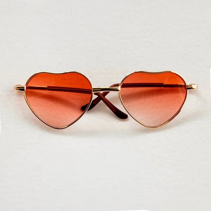 Heart-shaped sunglasses with orange lenses on a light gray background
