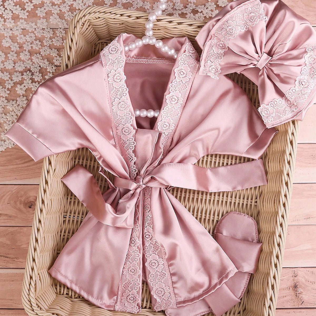 Pink satin robe with lace trim and matching headband on a woven basket.