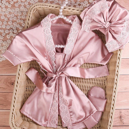 Pink satin robe with lace trim and matching headband on a woven basket.