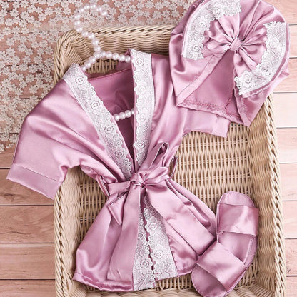 Pink satin robe with lace details and matching headband on a woven basket.