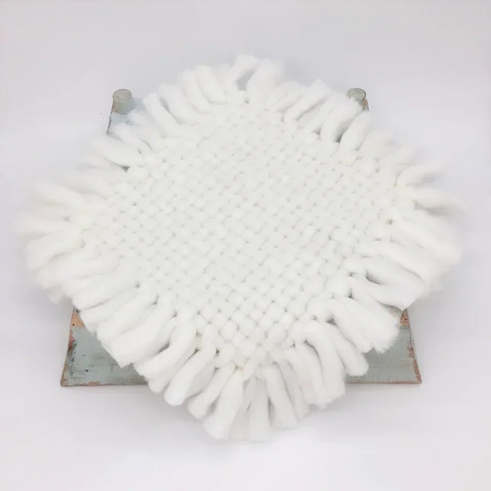 A round white fringed textile piece, likely a decorative mat or cushion cover, displayed on a distressed metal stand against a plain white background.