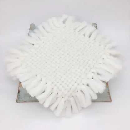 A round white fringed textile piece, likely a decorative mat or cushion cover, displayed on a distressed metal stand against a plain white background.