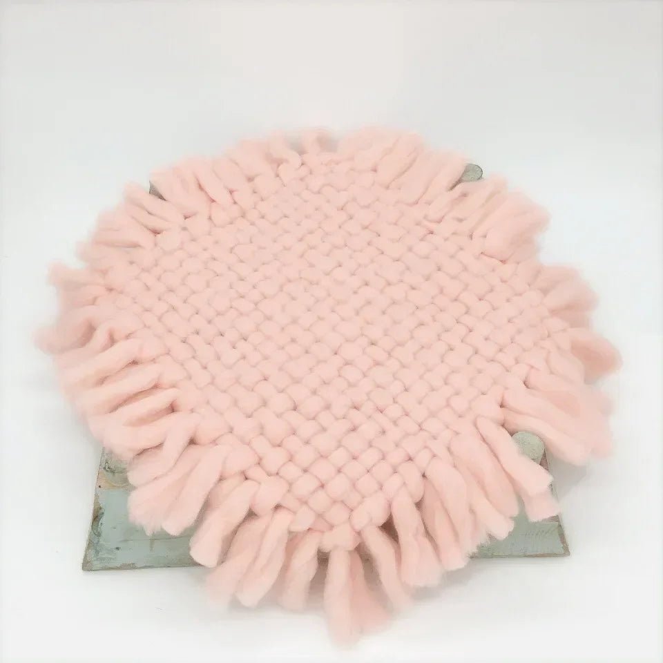 A round, light pink fringed microfiber cleaning cloth with a textured woven center, resting on a distressed gray wooden block against a white background.